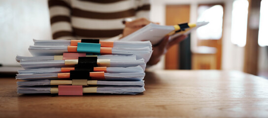 A person organizing stacks of documents with colorful binder clips on a wooden desk in a bright office environment.
