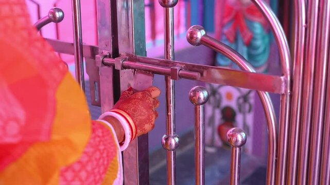 Authentic close-up footage of an Indian bride unlocking a temple gate during a traditional Hindu wedding ceremony. The bride's hands, decorated with mehndi (henna) and traditional bangles
