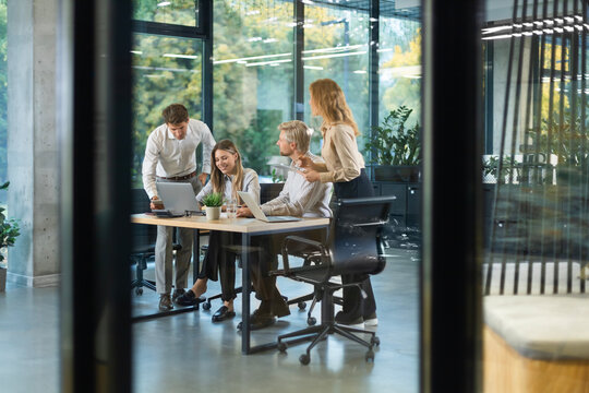 A modern office interior, featuring a blurred view of workers at desks, through a glass partition.