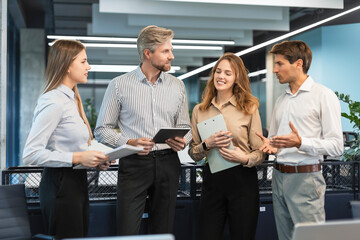 Group of business people standing together and discussing their work and projects, having a team meeting in an office.
