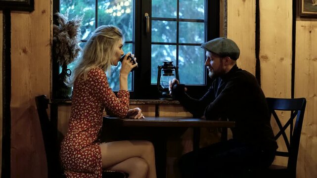 Engaging conversation between a blonde woman and a man in a flat cap at a wooden table, sharing drinks, camera pans to capture the intimate moment and ambiance