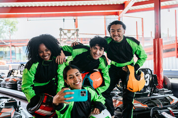 Young diverse friends wearing racing suits and helmets, smiling and taking a selfie at a karting track, enjoying a fun day