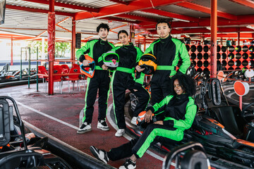 Obraz premium Diverse group of young adult friends wearing racing suits and holding helmets, preparing for a karting race at an outdoor track