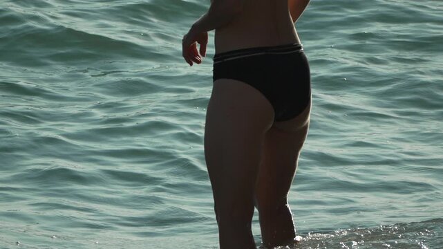 Woman Beach Water - A woman in a black bikini stands in the water at the beach.