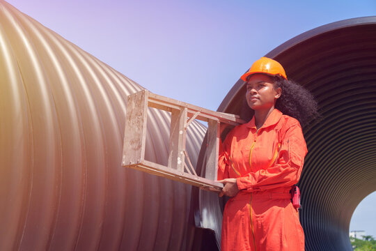 A female engineer in an orange uniform is inspecting the integrity and safety of a pipeline.