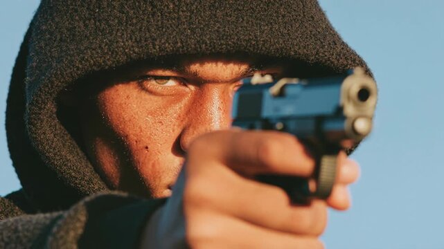 Hooded man points a handgun toward camera in tense close‑up; gritty dramatic scene representing danger, crime and confrontation for thriller trailers, security PSAs and social commentary on urban viol