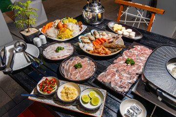 Hotpot meal outdoor setting with fresh seafood, sliced meats, vegetables. Asian dining experience,...