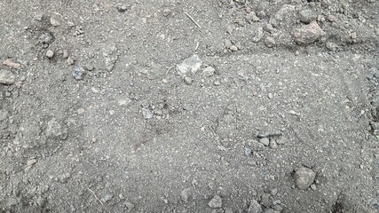 Detailed close-up texture of dark, uneven garden soil and dirt mixed with small stones and pebbles.