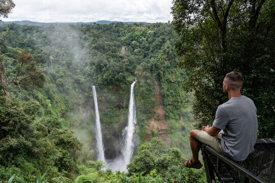 Man contemplating tad fane waterfall and jungle landscape