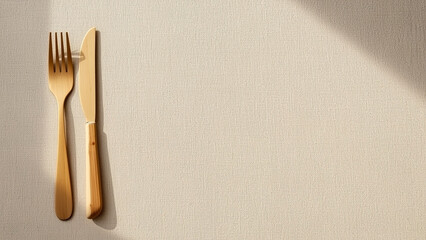 Golden cutlery set under sunlight on a beige tablecloth, flat lay style