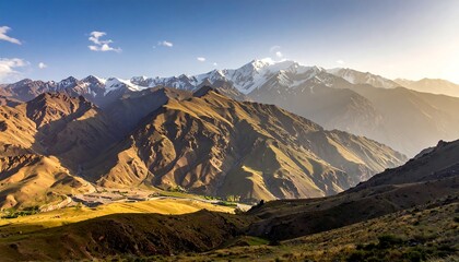 Rugged mountains under a blue sky, some with snow, bathed in golden light, seen from an elevated vantage point