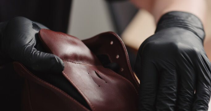 man hands in black gloves applying protective cream to brown leather sneakers