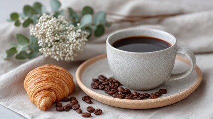 A Rustic Flat Lay of Roasted Coffee Beans and a Croissant Beside a Mug of Hot Coffee on a Textured Fabric Background with Eucalyptus Garnish Soft Natural Lighting