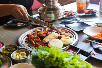Korea BBQ style restaurant. Asian traditional pickle vegetable ingredients on table with people grilling background.
