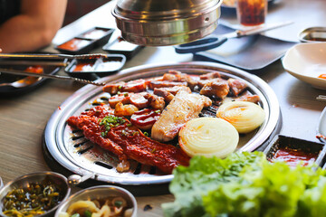 Korea BBQ style restaurant. Asian traditional pickle vegetable ingredients on table with people grilling background.
