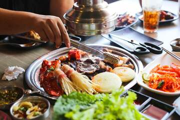 Korea BBQ style restaurant. Asian traditional pickle vegetable ingredients on table with people grilling background.
