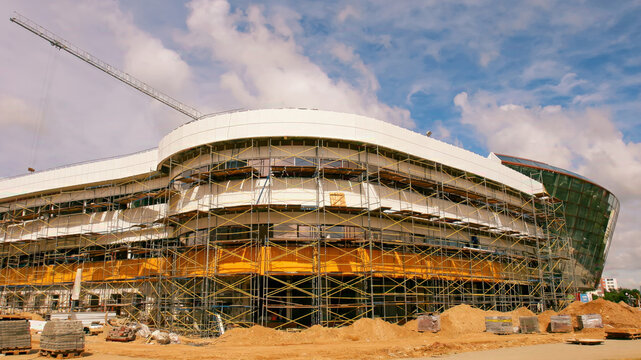 Construction of a modern stadium in a sunny location, showcasing scaffolding and heavy equipment