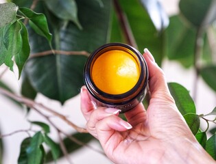 hand holding a jar of orange cleansing balm