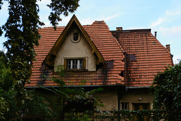 Old vintage house with red roof, attic window and decorative wooden details surrounded by greenery