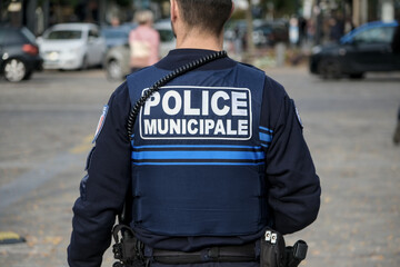 A municipal police officer seen from behind wearing a blue uniform and radio equipment while...
