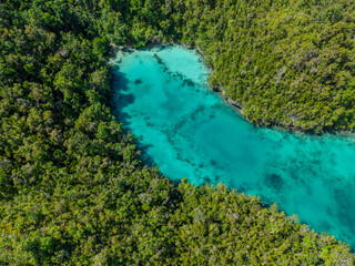Aerial view of calm blue lagoon surrounded by lush green tropical islands in Raja Ampat, Indonesia.  
