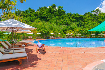 sun umbrellas and beds by the swimming pool at a luxury resort in nature in summer. Landscape with a outdoor pool with blue water in hotel. Vacation and relaxation. Destination for tourism