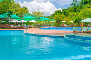 sun umbrellas and beds by swimming pool at luxury resort in nature in summer. Landscape with...