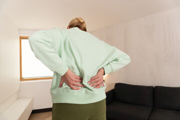 Person feeling pain in the lower back and touching spine area indoors. Concept of muscle strain, posture issue, and physical health. Focus on wellness, prevention, and daily recovery.