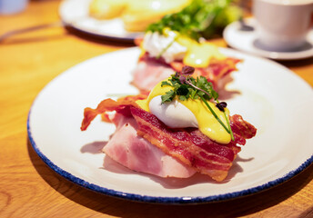 Egg benedict. Poached egg, bacon, ham, hollandaise sauce, onion on slice toast for tasty breakfast. close up. English brunch.
