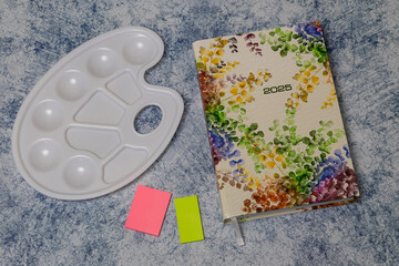 Watercolor palette beside a vibrant 2025 planner with sticky notes, showcasing artistic tools and organization for creative projects and planning ahead