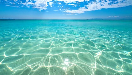 Shimmering, turquoise sea reflects sunlight, creating abstract patterns under a bright blue sky with fluffy white clouds