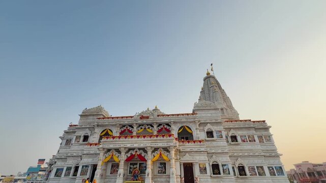 Side view of Prem Mandir temple showing the full expanse of its marble structure and twin domes under a clear sky. This iconic Hindu temple stands as a symbol of divine love and spiritual grandeur in 