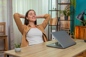 Young woman sitting at home table closes laptop then leans back stretching arms and feeling deep relief after work. Caucasian girl smiles softly appreciating finished tasks and quiet victory celebrate