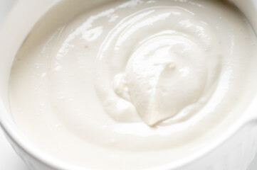 Close-up, high-angle shot of a thick, creamy white substance with smooth swirls in a white bowl, against a neutral white background