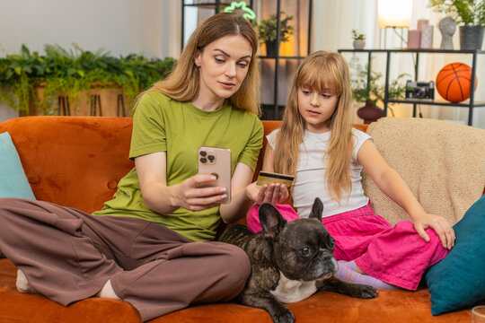 Mother and daughter with French bulldog at home learn safe online card payment set rules and limit. Woman and girl with dog on sofa show okay gesture teach security steps avoid fraud confirm lesson