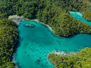 Aerial view of calm blue lagoon surrounded by lush green tropical islands in Raja Ampat, Indonesia.  
