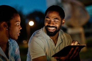 Portrait of young happy couple using tablet computer at night, using modern technology having fun with glowing screen in dark outdoors in the city