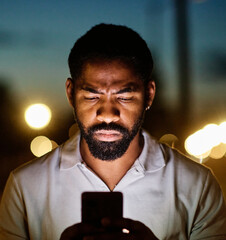 Focused man using smartphone outdoors during twilight with city lights in the background