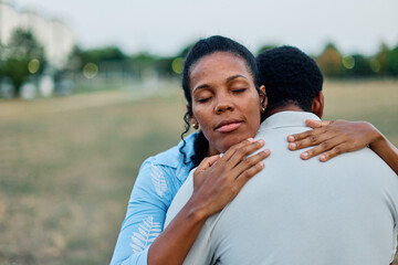A couple shares a warm embrace in a park during sunset, displaying affection and intimacy, portrait of a young black woman