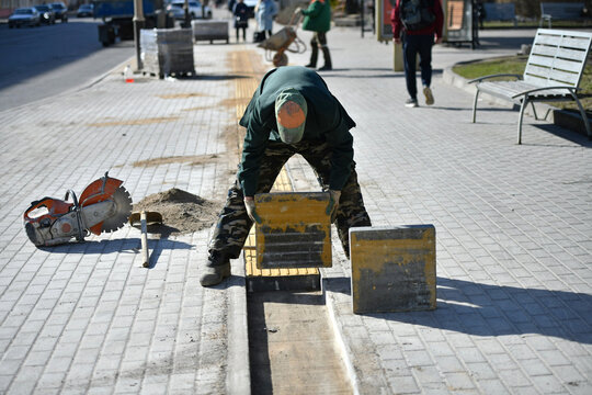 A worker lays a concrete block on a city street.