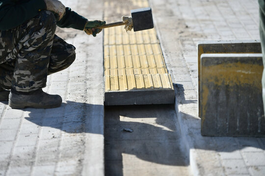 A worker levels a concrete road tile with a hammer.