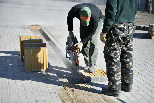 A worker cuts with a circular saw, construction work on a city street.