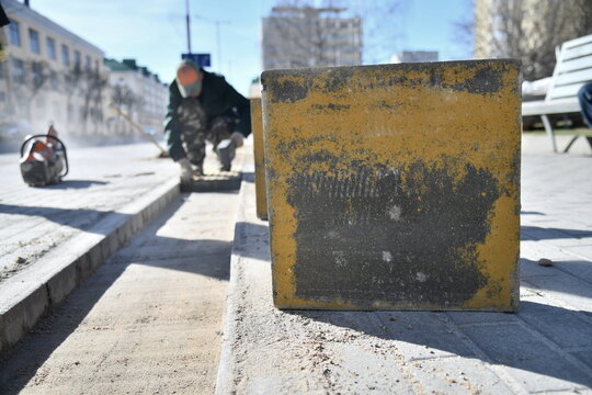 A concrete block in close-up!A worker lays tiles on a city street.