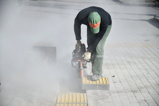 A worker is sawing a road curb, there is a lot of dust.
