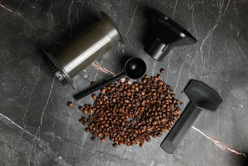 Coffee press with hot coffee and roasted beans on a dark background