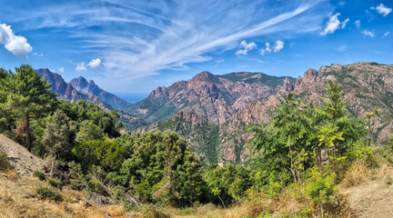panoramic view of the village of porto ota and the mountainous landscape towards the Gulf of Porto in sunlight with blue skies and spectacular clouds	