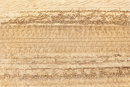 Closeup of vehicle tire tracks on dry sandy soil showing texture and pattern. Symbol of travel, adventure, and off-road driving. Background for transportation, journey or desert road.