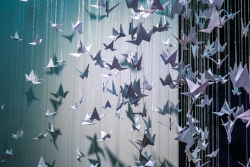 paper origami birds tied to strings hanging in air against a black background. The paper origami birds vary in size and orientation, creating a dynamic, three-dimensional effect