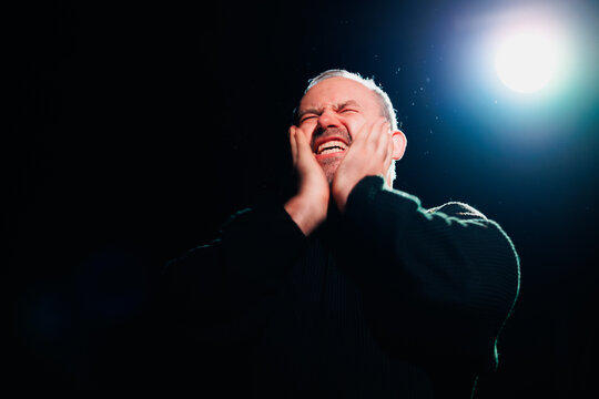 Emotional actor performing on theater scene with spotlight 