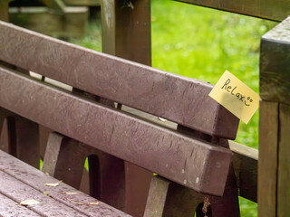 Handwritten Relax Note with Smiley Face Tucked into Wooden Park Bench Outdoors